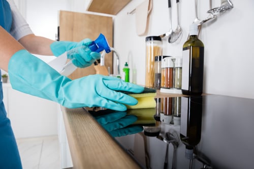 Janitor Cleaning Kitchen Worktop With Sponge And Spray Bottle  A